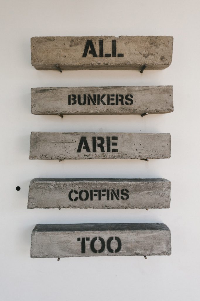 Concrete blocks stencilled 'All bunkers are coffins too' at Neverland's 'Apocalypse Luxe' exhibition